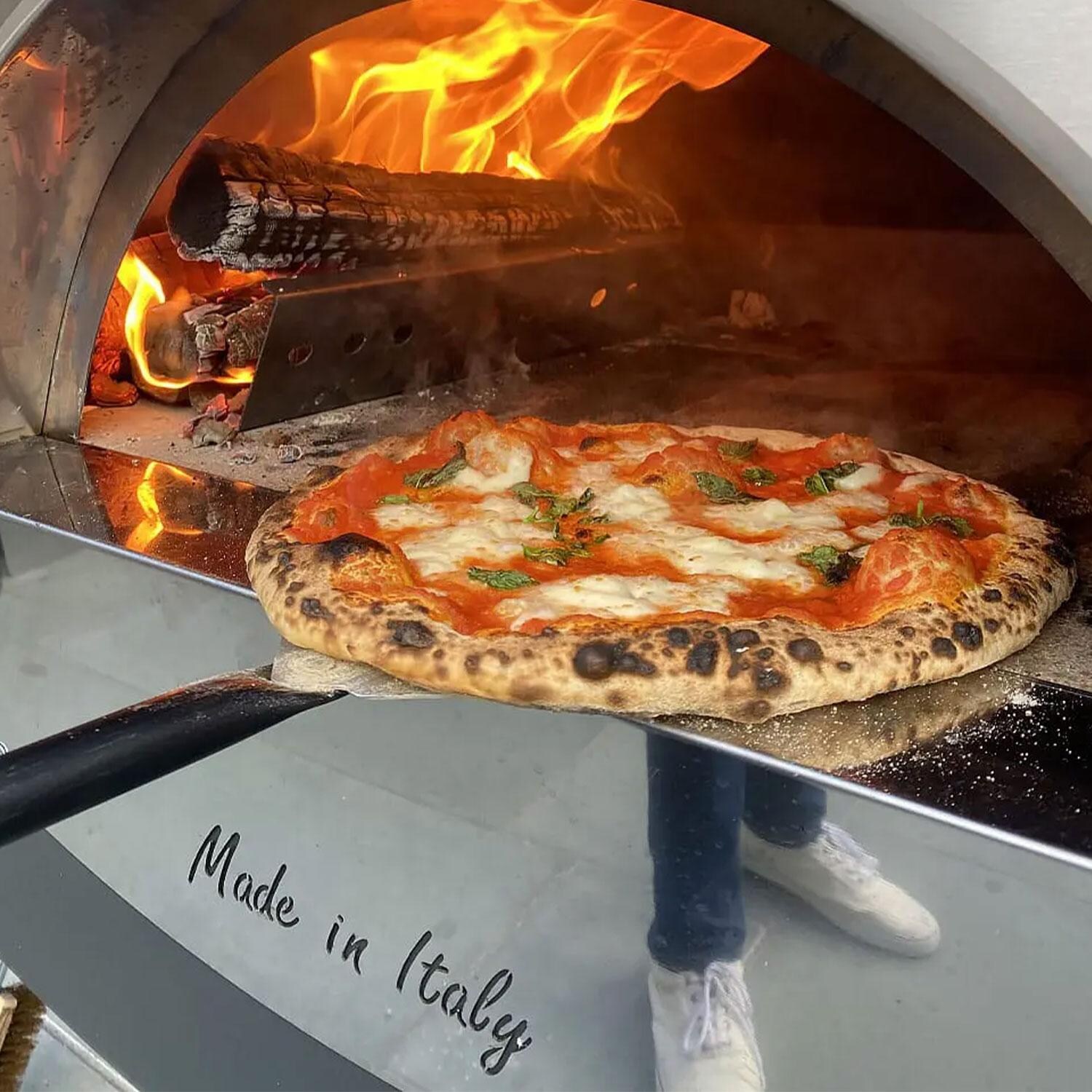 XO Appliance XOPIZZA2FSCA PIZZA2 Wood-Fired Pizza Oven in Carbona - Placing Pizza in Oven - Lifestyle thumbnail