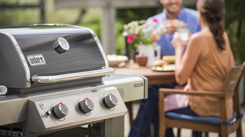 Freestanding Weber gas grill with couple dining in the background