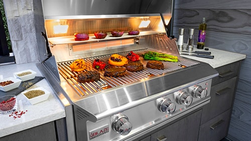 built-in Blaze Pro LUX gas grill cooking steak with red onions on the warming rack