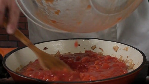 Tomato mixture being added to the cooked onions, to be cooked down