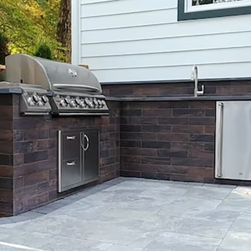 Angled view of the small stone-clad counter space showing the sink, grill, and refrigerator