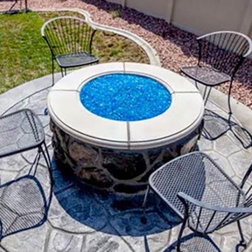 Circle fire pit clad with stone and filled with blue fire glass