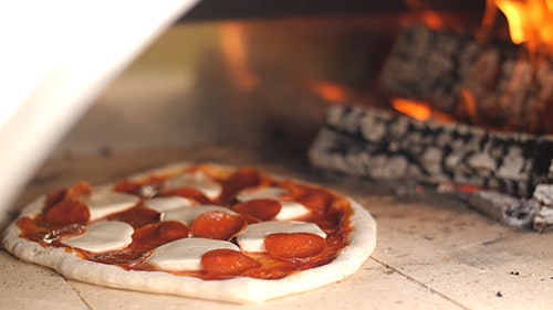 Pizza cooking next to a stack of wood in an oven