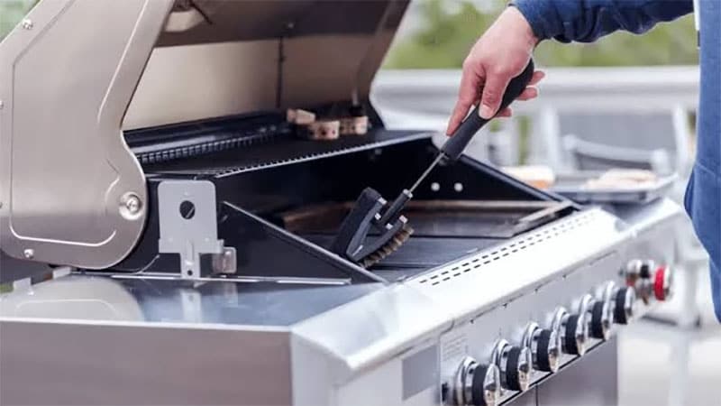 using a grill brush to clean the grates of a stainless steel gas grill