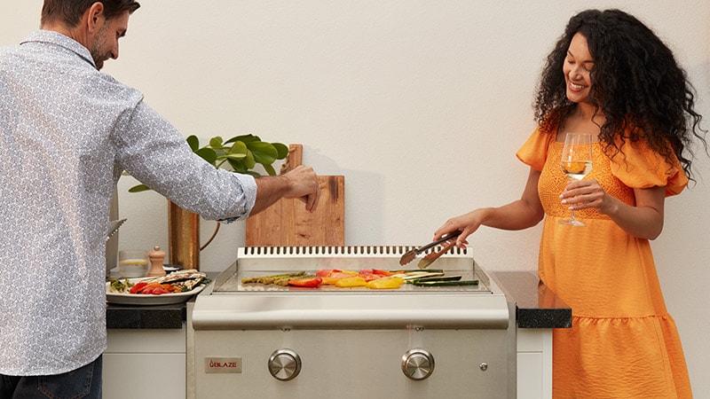 Couple grilling vegetables on their built-in Blaze gas griddle