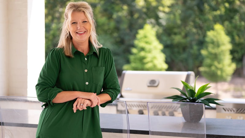 Angie smiling in front of an outdoor kitchen with Napoleon gas grill