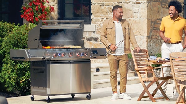 Men standing near an open gas grill with food cooking