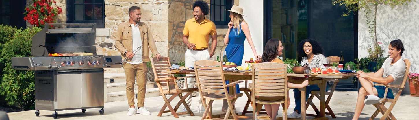 People standing around an open gas grill and outdoor patio dining table and chairs
