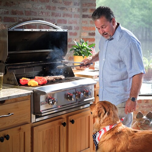 Man standing in front of open built-in gas grill with dog