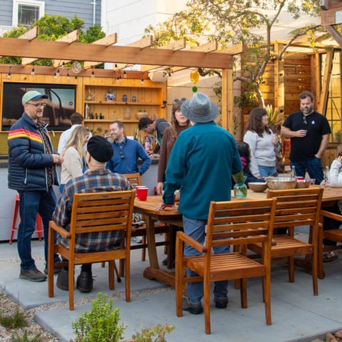 people sitting and standing around an outdoor entertainment space with TV