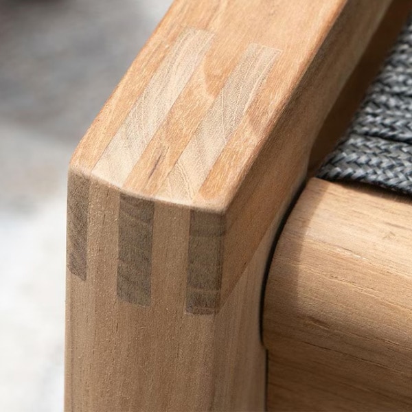 Close-up photograph of a teak chair arm showing precision mortise-and-tenon construction and a smooth, flush fit