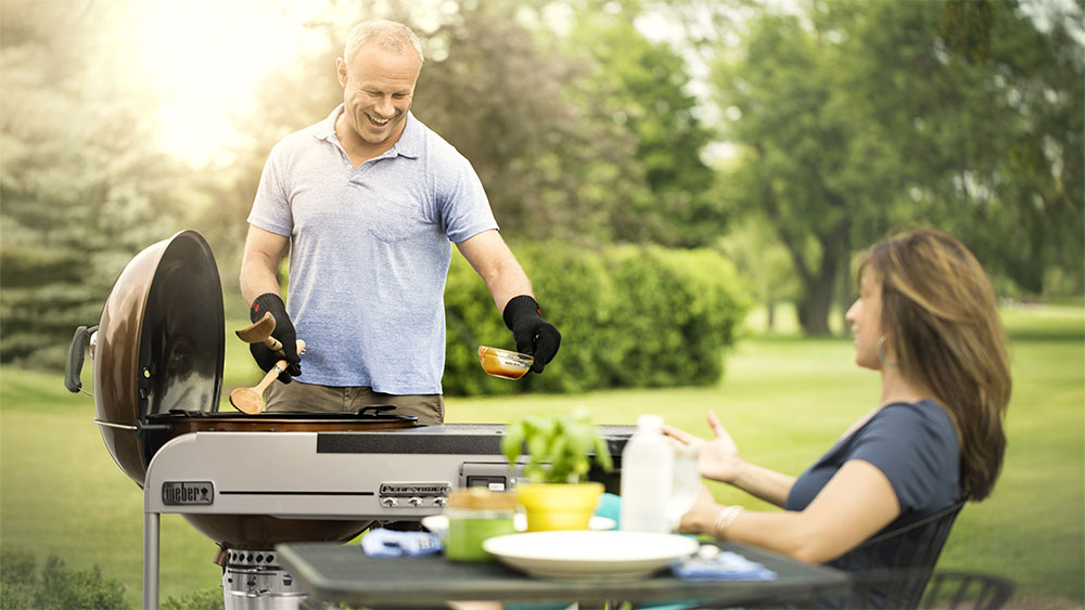 Man cooks food on Weber Performer grill while woman sits at table