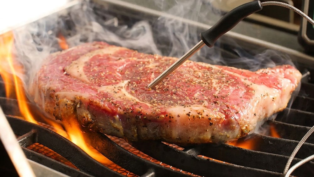 steak cooking on a grill with meat thermometer inserted