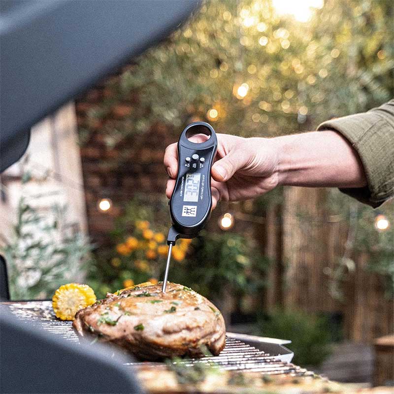 woman using instant read thermometer to check temperature of chicken on a grill