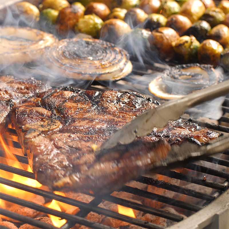 steaks, onions, and potatoes cooking on a grill