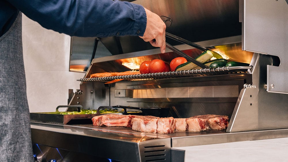 man cooking steaks and vegetables on a gas grill