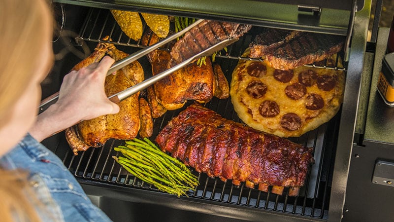 man tending to a pellet grill stuffed with different foods cooking