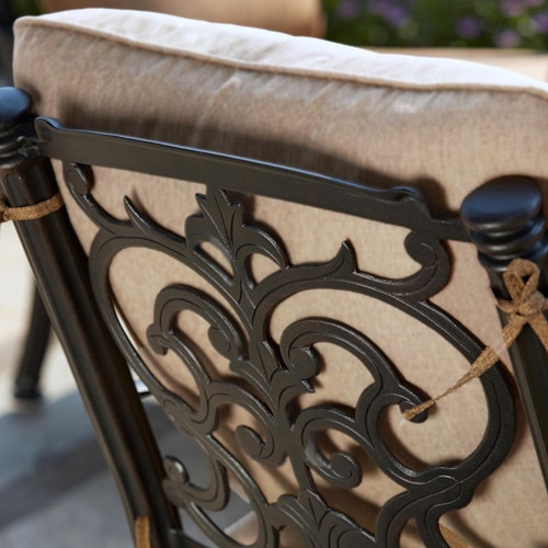 Close-up of an aluminum chair back with ornate scroll detailing and a tan cushion