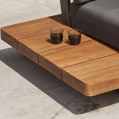 Close-up of a teak wood coffee table with two glasses, beside a gray outdoor sofa