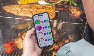 Turkey breast and ham on a smoker with wireless probes while the cook checks temperatures on a phone