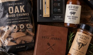 Flat lay of specialty grilling gifts including wood chunks, a wireless thermometer, BBQ sauce, a grill journal, and spice rub