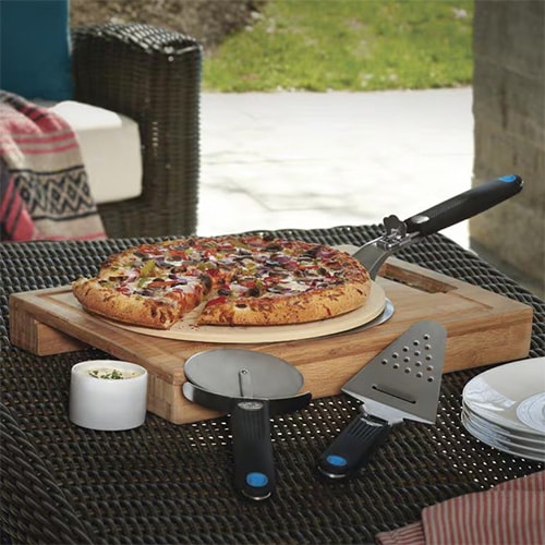 Fresh pizza on pizza stone with pizza cutter, spatula, and pizza peel