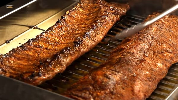 flipping over seasoned rib racks on the grill